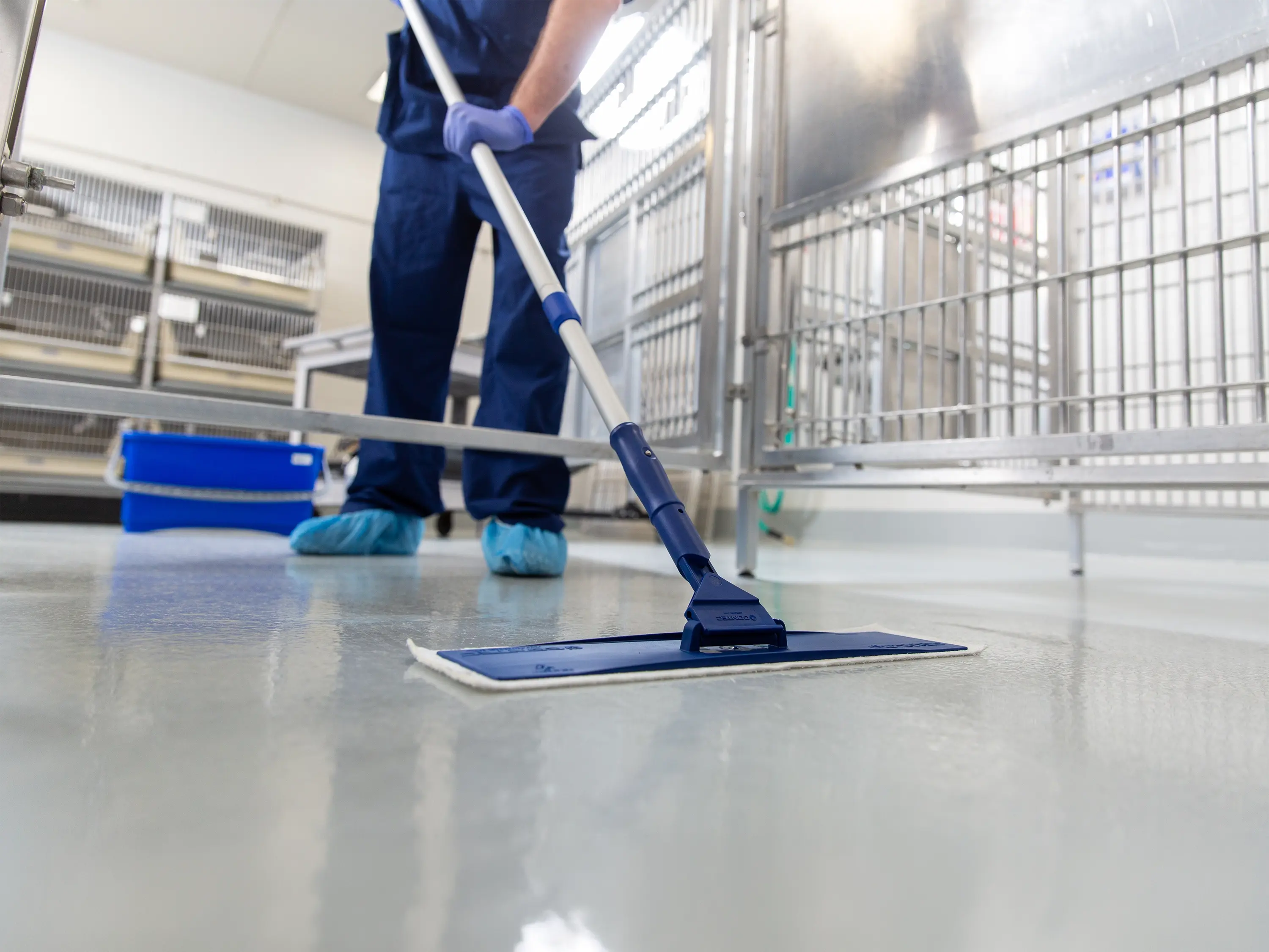 Worker using a flat mop to clean the floor in a controlled facility with stainless steel equipment.